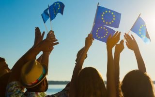 Miksi kannattaa rekisteröidä vaihtoehtoisia verkkotunnuksia? Kuvassa ihmisiä rannalla heiluttamassa EU:n lippuja.